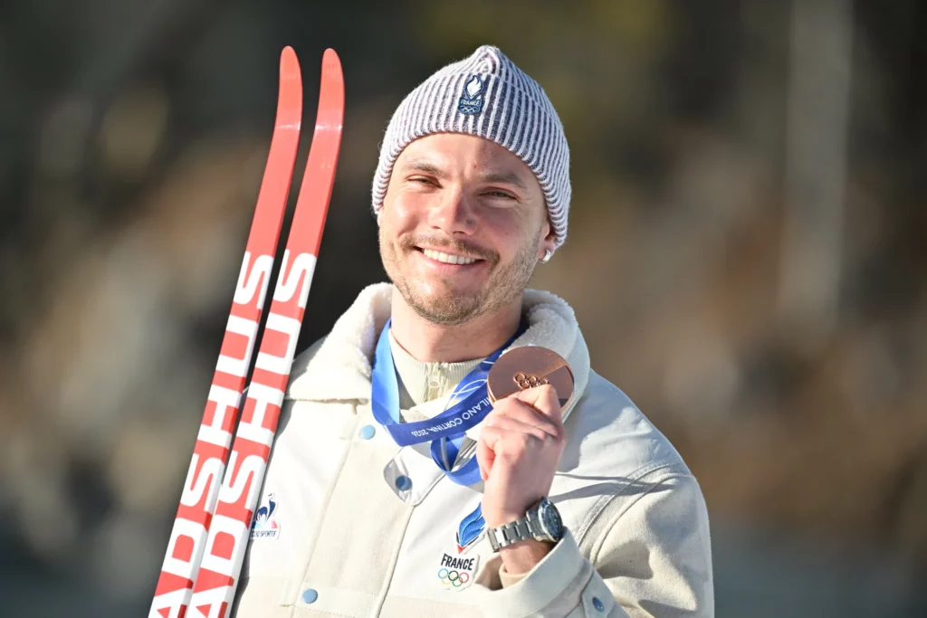Emilien Jacquelin montre sa médaille de bronze et pose avec ses skis aux JO de Milano-Cortina