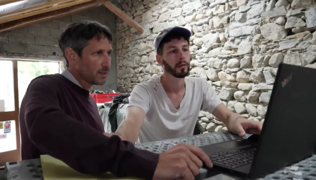 Deux personnes regardent l'écran d'un ordinateur dans une maison avec pierres apparents en cours de rénovation énergétique