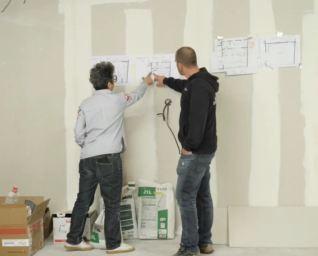 Deux personnes de dos, un homme et une femme, regardent des instructions affichées sur un mur en cours de rénovation