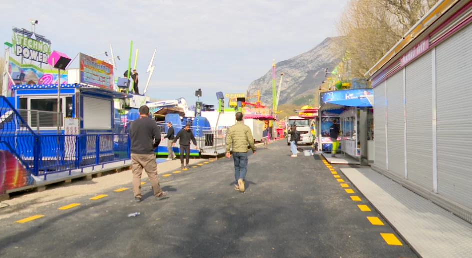 La foire des rameaux sur un sol provisoire avec des bandes jaunes en pointillé, des forains travaillent sur leur manège