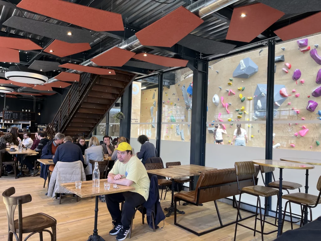 Des personnes attablées dans le restaurant de l'orangerie perchée à Grenoble, avec la salle d'escalade en arrière plan