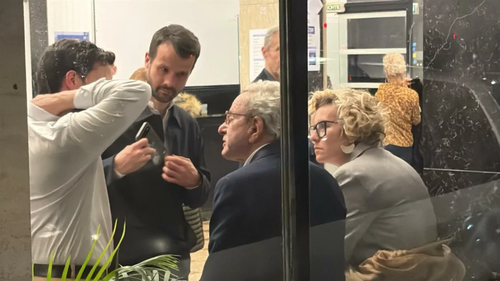 Alain Carignon, de dos, derrière une vitre dans son QG de campagne à Grenoble avec ses colistiers Emilie Chalas et Pierre-Edouard Cardinal